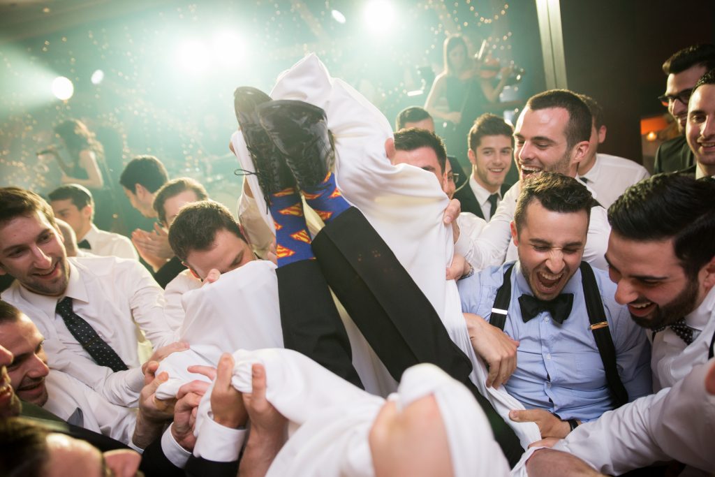 Groom with superman socks surrounded by groomsmen in the horah